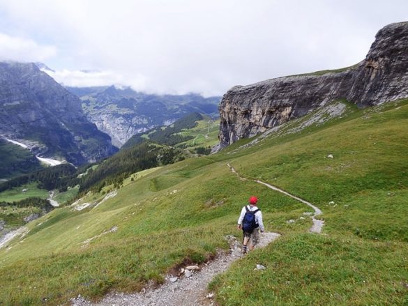 moški z rdečo kapo hodi po gorski poti nad dolino Lauterbrunnen