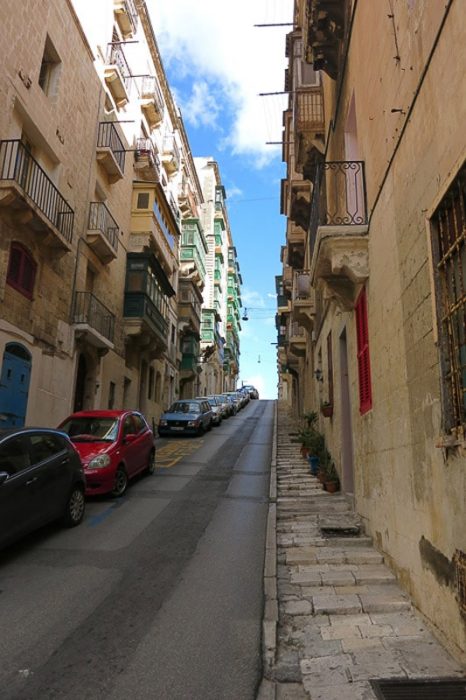 ozka ulica speljana v klanec. ob eni strani so parkirani avtomobili, na obeh straneh se dvigujejo visoke starinske hiše