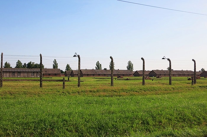 travnik in visoka ograda. na drugi strani stojijo barake Birkenau-a