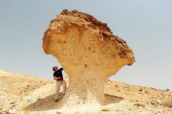 moški stoji ob skalni strukturi. puščavska goba v bližini Wadi Daykah, oman