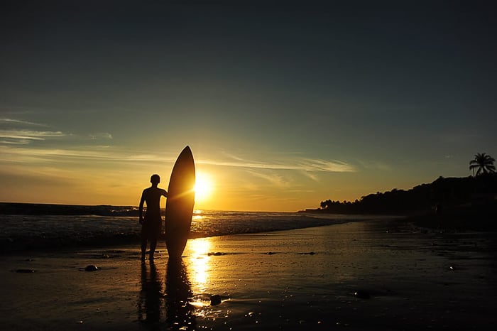 moški s surfom ob sončnem zahodu