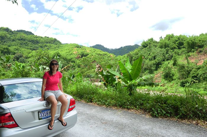 Ženska sedi na avtomobilu, v ozadju je bujno tropsko rastje