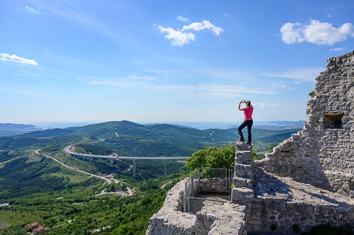 ženska stoji na ruševinah črnokalskega gradu, v ozadju viadukt, hribi in morje