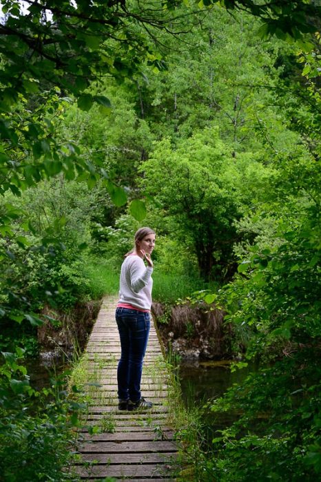 ženska na lesenem mostu v zelenem gozdu
