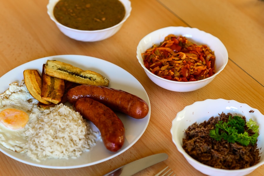 kolumbijska hrana: bandeja paisa. NA krožniku je pečena banana, klobasa, jajce in riž, v skodelicah pa omaka iz fižola, paradižnika in govedina