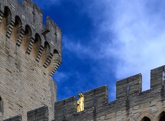 grajsko obzidje skozi katerega se vidi zlati kip marije