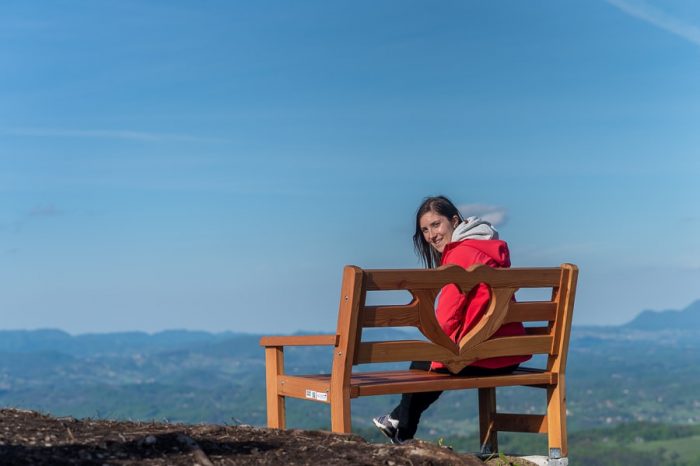 ženska sedi na klopci ljubezni z razgledom na hribovito pokrajino Kozjansko