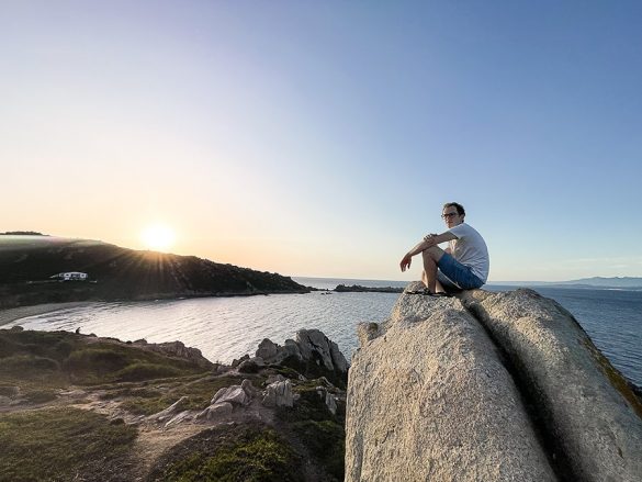 moški sedi na skali nad plažo Rena Bianca in opazuje sončni zahod