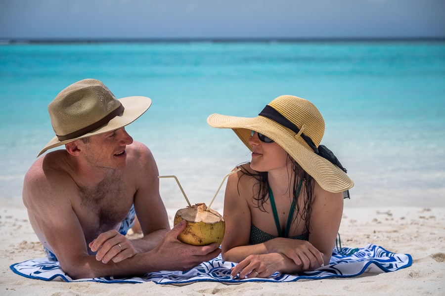 moški in ženska s kokosom v roki ležita na plaži