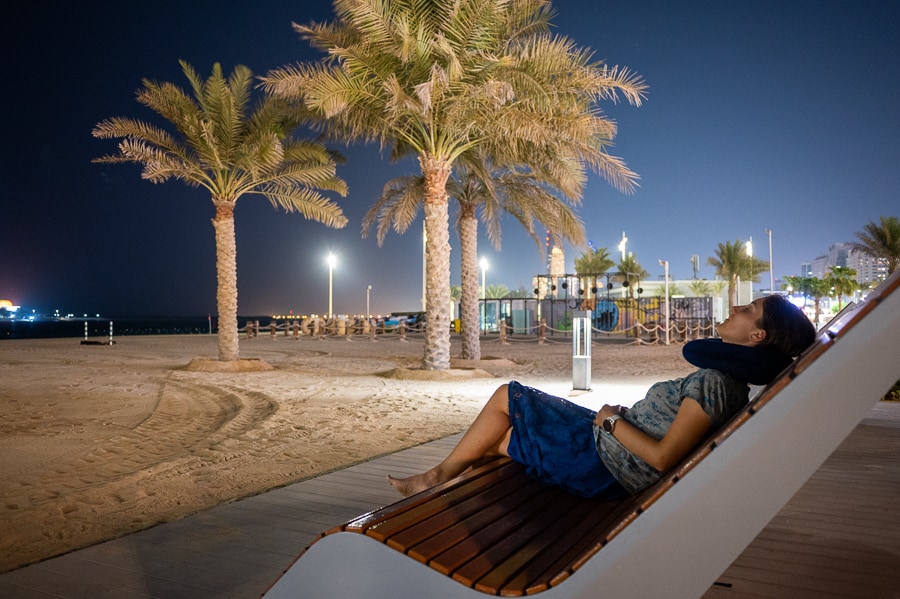 ženska na plaži - sedi na stolu pod palmo. Corniche Abu Dhabi