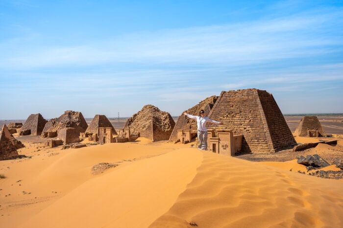 sudanske piramide Meroe, spredaj pa stoji ženska v beli srajci